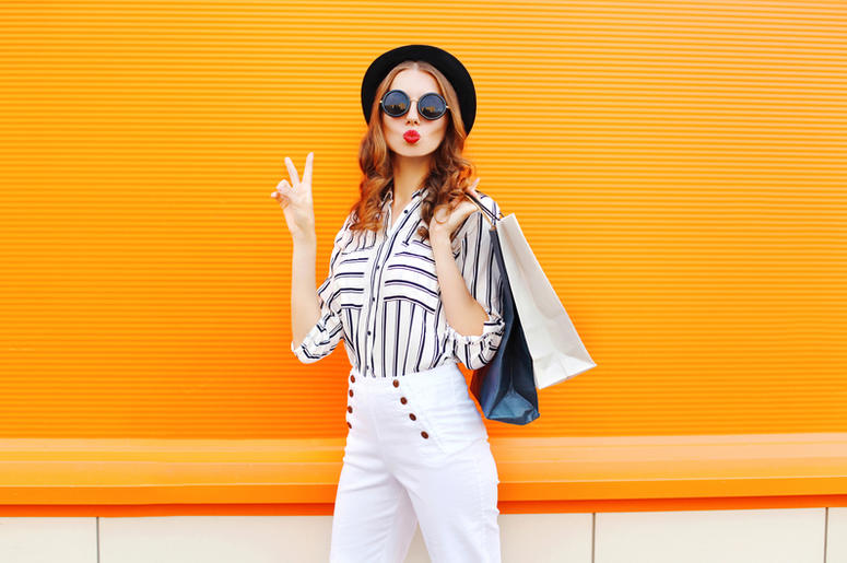 Fashion young girl with shopping bags wearing a black hat white pants over colorful orange Fashion young girl with shopping bags wearing a black hat white pants over colorful orange