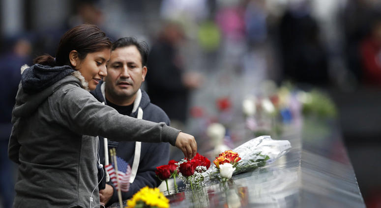 A woman drips water on a bouquet of flowers at the North Pool during a ceremony marking the 17th anniversary of the terrorist attacks on the United States on Tuesday, Sept. 11, 2018, in New York. (AP Photo/Mark Lennihan)
