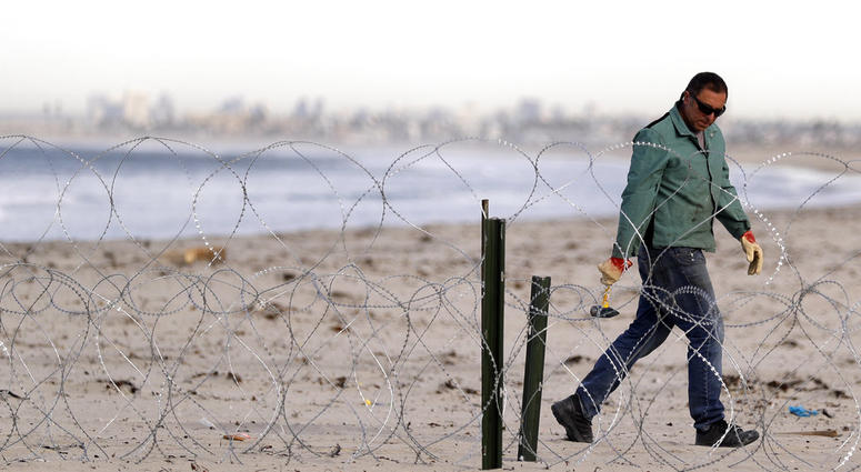 A worker installs concertina wire along the beach closest to the border, as the city of San Diego sits in the distance, as seen from Tijuana, Mexico, Wednesday, Nov. 14, 2018. (AP Photo/Gregory Bull)