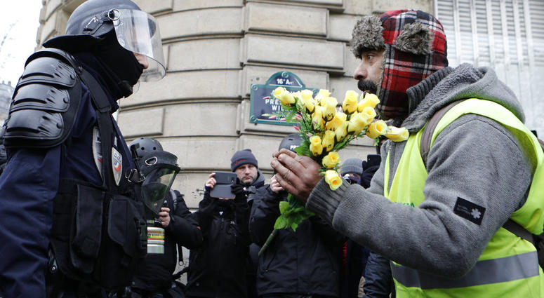 A demonstrator wearing his yellow vest holds a bouquet of roses in front of a riot police officer during a protest Saturday, Dec. 15, 2018 in Paris