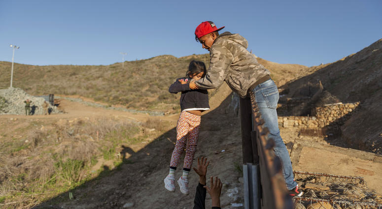 A migrant from Honduras pass a child to her father after he jumped the border fence to get into the U.S. side to San Diego, Calif., from Tijuana, Mexico, Thursday, Jan. 3, 2019.