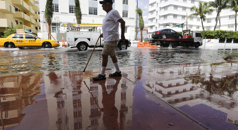 In this Sept. 30, 2015 file photo, Louis Fernandez walks along a flooded street in Miami Beach, Fla. (AP Photo/Lynne Sladky, File)