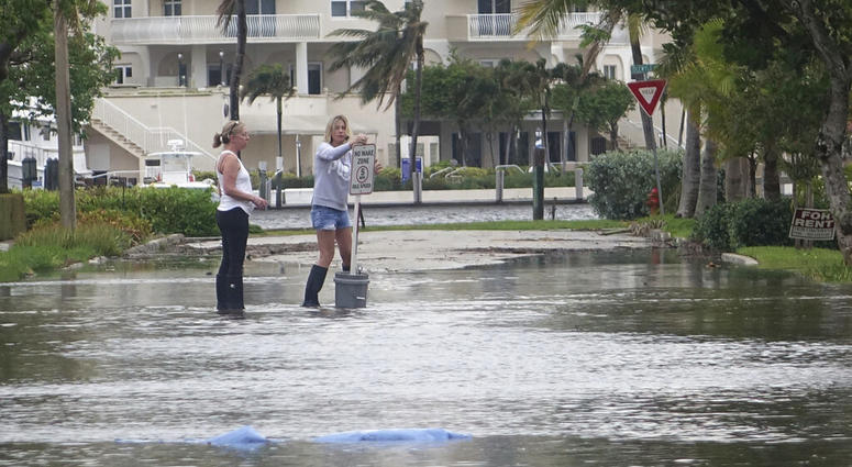 In this Oct. 5, 2017, file photo, residents move a "no wake," sign through flood waters caused by king tides in Fort Lauderdale, Fla. (Joe Cavaretta/South Florida Sun-Sentinel via AP)
