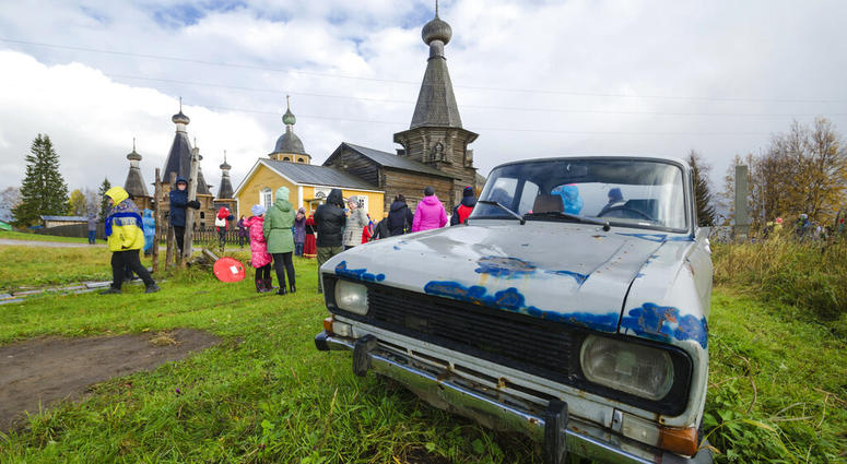 In this photo taken on Oct. 7, 2018, people walk the street with the 18th century Trinity Church in the background in the village of Nyonoksa, northwestern Russia. (AP Photo/Sergei Yakovlev)