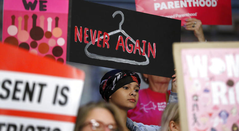 In this Tuesday, May 21, 2019 file photo, August Mulvihill, of Norwalk, Iowa, center, holds a sign depicting a wire clothes hanger during a rally at the Statehouse in Des Moines, Iowa, to protest recent abortion bans. (AP Photo/Charlie Neibergall)