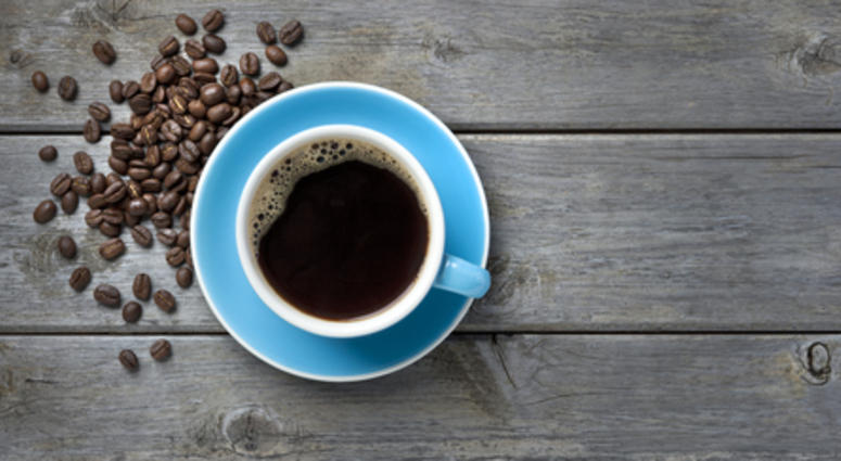 A blue coffee cup full of black coffee on a wood background with coffee beans
