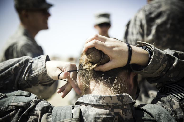 Spc. Nina Bray, intelligence analyst, Headquarters and Headquarters Company, 204th Brigade Support Battalion, 2nd Armored Brigade Combat Team, 4th Infantry Division, fixes her hair bun before putting on her body armor at a M203/M320 40 mm grenade launcher