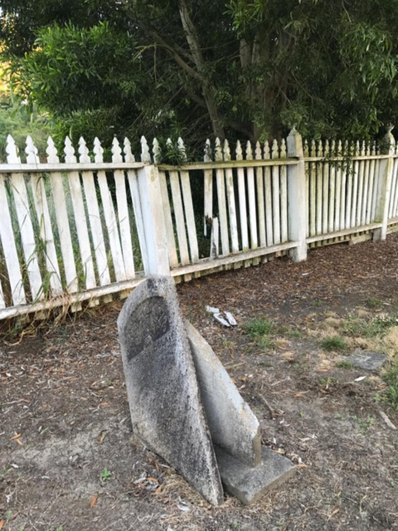 A headstone in pieces is pictured next to a fence in disrepair. stones