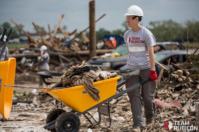 A Team Rubicon volunteer wheels away debris from a home.