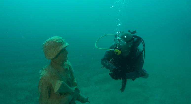 A diver comes face-to-face with one of 12 life-size statues of members of the Armed Forces that make up the Circle of Heroes underwater veterans memorial. DiverStatue
