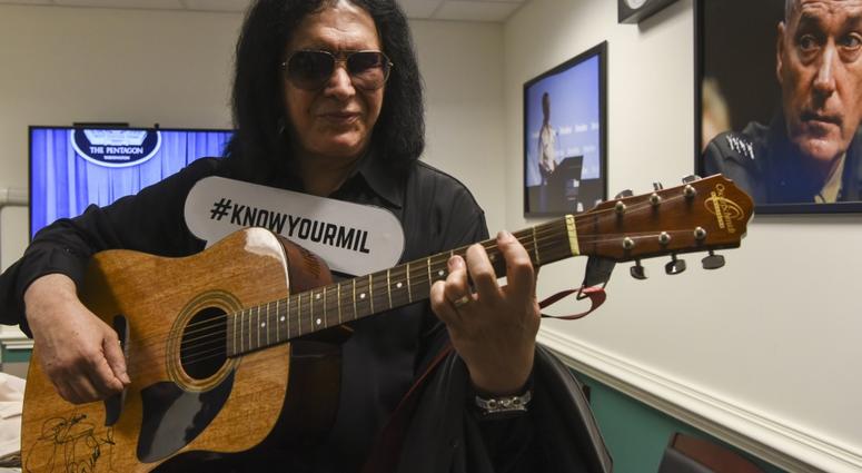 Gene Simmons of KISS strums a guitar while displaying a sign with the Department of Defense's #KnowYourMil hashtag, following a meet and greet with service members and civilians, at the Pentagon, Washington, D.C., May 16, 2019. GeneSimmonsPentagon6