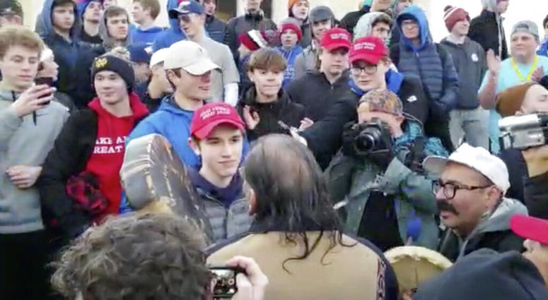In this Friday, Jan. 18, 2019 image made from video provided by the Survival Media Agency, a teenager wearing a "Make America Great Again" hat, center left, stands in front of an elderly Native American singing and playing a drum in Washington. In this Friday, Jan. 18, 2019 image made from video provided by the Survival Media Agency, a teenager wearing a "Make America Great Again" hat, center left, stands in front of an elderly Native American singing and playing a drum in Washington.
