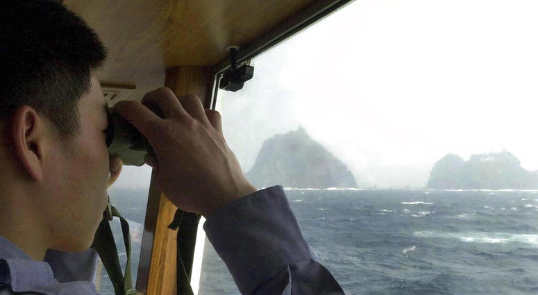 In this April 28, 2005, file photo, a South Korean coast guard looks at Dokdo islets, known as "Takeshima" in Japanese, through a telescope on the patrol ship Sambong-ho on the East Sea, South Korea. AP DO NOT USE