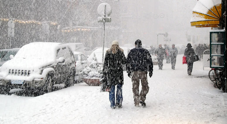 People walking down sidewalks in a snow storm in a city People walking down sidewalks in a snow storm in a city