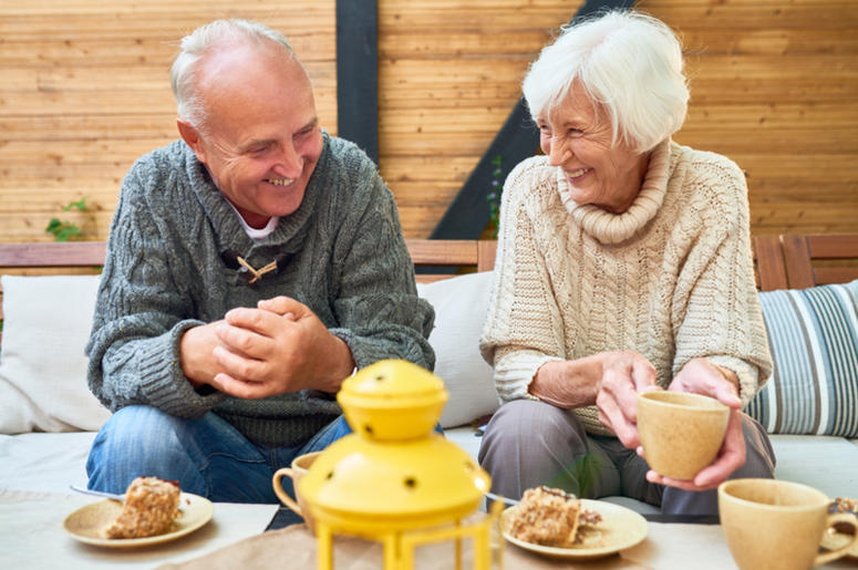 Portrait of happy senior couple laughing heartily enjoying time together in retirement sitting at table in outdoor cafe drinking coffee with cakes