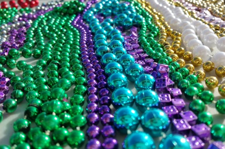Purple green blue gold and white beads from New Orleans Mardi Gras celebration. View is level with the objects and perspective is moving away from camera. These are long strands of round beads.