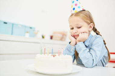 Sad birthday - Sad little girl in birthday cap looking at festive cake with candles Sad birthday - Sad little girl in birthday cap looking at festive cake with candles