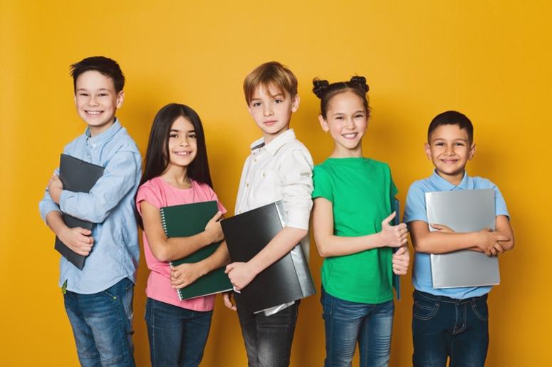 School kids with notebooks, standing in row and looking at camera over yellow background School kids with notebooks, standing in row and looking at camera over yellow background