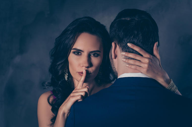 (Deagreez/ iStock/ Getty Images Plus) Couple in romantic embrace, woman shushes the viewer