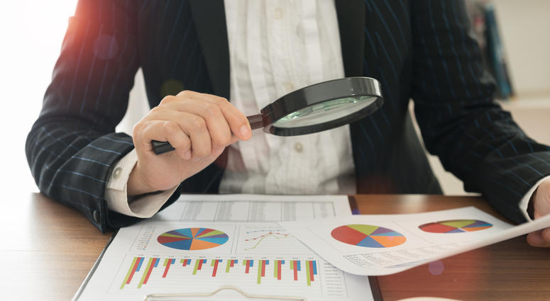 Auditor uses magnifying glass to look over financial papers