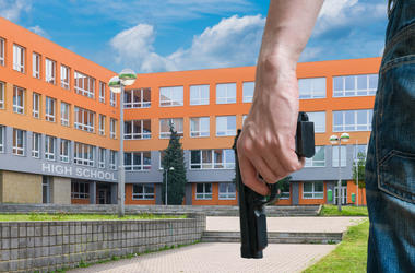 Criminales Inician Balacera Al Esconderse En Escuela Gun control concept. Young armed man holds pistol in hand in public place near high school.