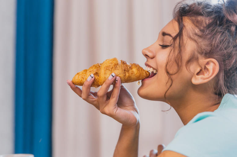 Ramilletes Hechos de Cuernitos Para El Baile De Graduación Photo of a cheerful young woman happy. Going to the table and eating croissant.