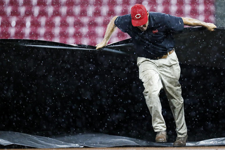 A member of the grounds crew helps pull a tarp onto the infield during a rain delay in the third inning o