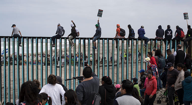 Border Central American migrants traveling with a caravan gather at the border wall, some sitting on top of it, look toward the U.S. from Mexico during a gathering of migrants living on both sides of the border, on the beach where the border wall ends in the oce