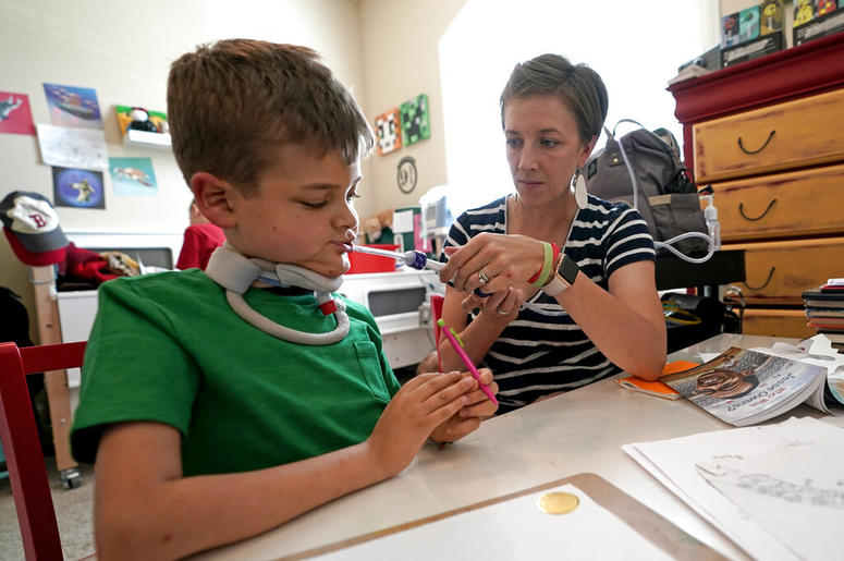 Rachel Scott, right, helps suction the mouth of her son, Braden, in Tomball, Texas on Friday, March 29, 2019. He was 7 on July 4, 2016, when he uncharacteristically decided he didn’t want to go swimming. He had trouble swallowing and felt tired and weak.