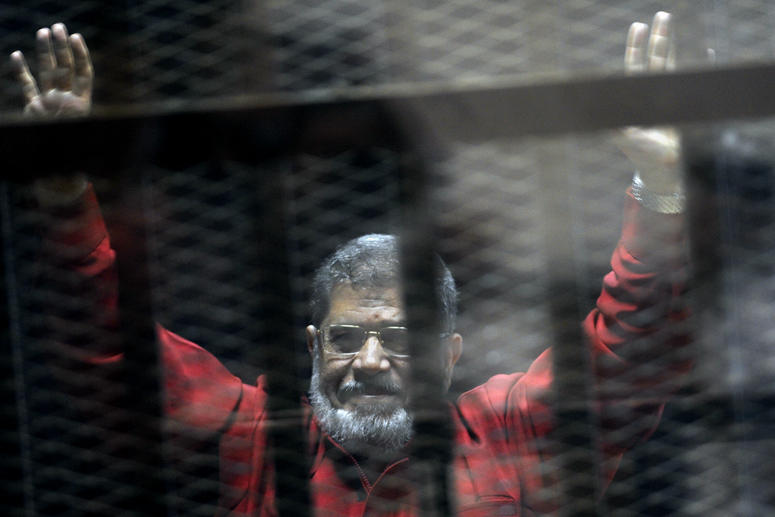 Former Egyptian President Mohammed Morsi, wearing a red jumpsuit that designates he has been sentenced to death, raises his hands inside a defendants cage in a makeshift courtroom at the national police academy, June 21, 2015, Cairo, Egypt. Egyptian President Mohammed Morsi