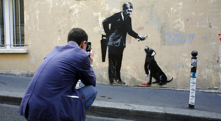 A man takes a picture of a graffiti believed to be attributed to street artist Banksy, in Paris. A man takes a picture of a graffiti believed to be attributed to street artist Banksy, in Paris.