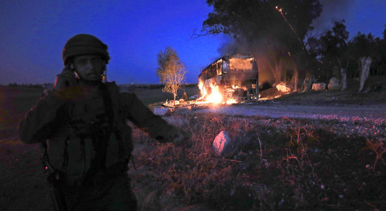 An Israeli soldier stands near a burning bus after it was hit by a mortar shell fired from Gaza near the Israel Gaza border, Monday, Nov. 12, 2018. An Israeli soldier stands near a burning bus after it was hit by a mortar shell fired from Gaza near the Israel Gaza border, Monday, Nov. 12, 2018.