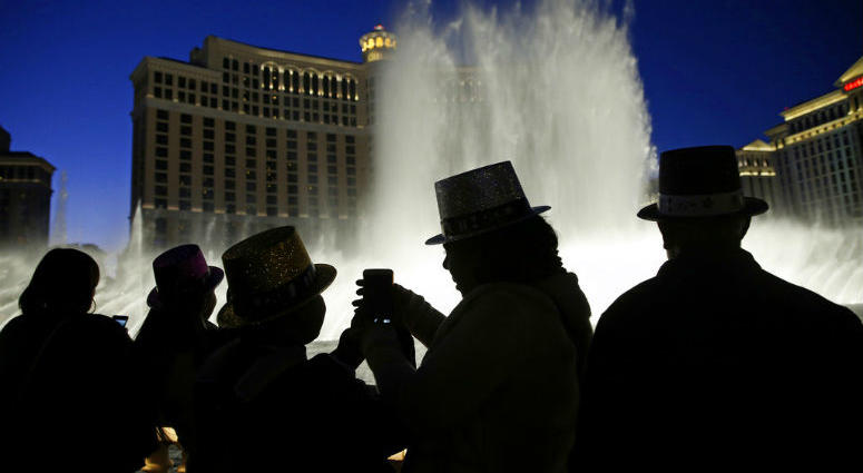 FILE - In this Dec. 31, 2015, file photo, people watch the fountains at the Bellagio while wearing paper hats to celebrate New Years Eve in Las Vegas. FILE - In this Dec. 31, 2015, file photo, people watch the fountains at the Bellagio while wearing paper hats to celebrate New Years Eve in Las Vegas.