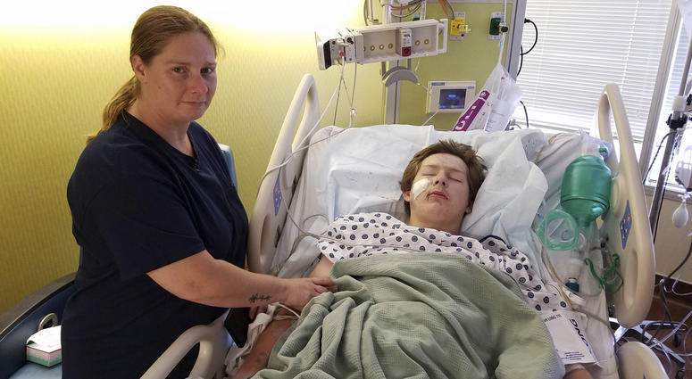 In this June 14, 2019 photo, 15-year-old Eli Gregg, right, recovers in the hospital bed in Kansas City, Kan., as his mother Jimmy Russell watches after doctors removed a 10" knife that impaled his face when he fell while playing. Eli Gregg