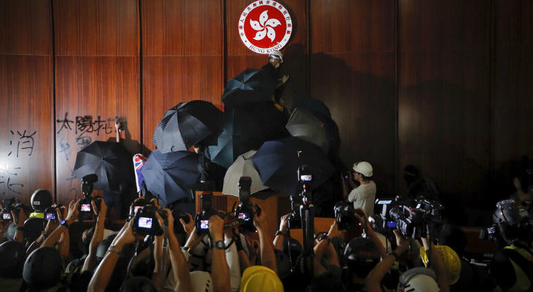 FILE - In this file photo taken Monday, July 1, 2019, journalists film a protester about to deface the Hong Kong emblem inside the meeting hall of the Legislative Council in Hong Kong. Protesters in Hong Kong took over the legislature's main building Monday night, tearing down portraits of legislative leaders and spray painting pro-democracy slogans on the walls of the main chamber.
