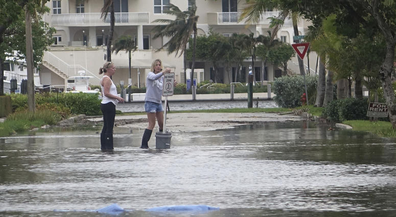 In this Oct. 5, 2017, file photo, residents move a "no wake," sign through flood waters caused by king tides in Fort Lauderdale, Fla. Flooding