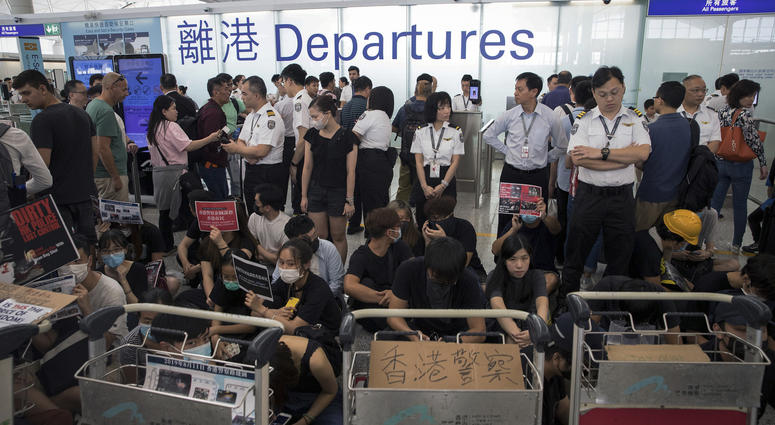 Airport security personnel stand guard as travelers walk past protesters holding a sit-in rally at the departure gate of the Hong Kong International Airport in Hong Kong, Tuesday, Aug. 13, 2019. Airport security personnel stand guard as travelers walk past protesters holding a sit-in rally at the departure gate of the Hong Kong International Airport in Hong Kong, Tuesday, Aug. 13, 2019.