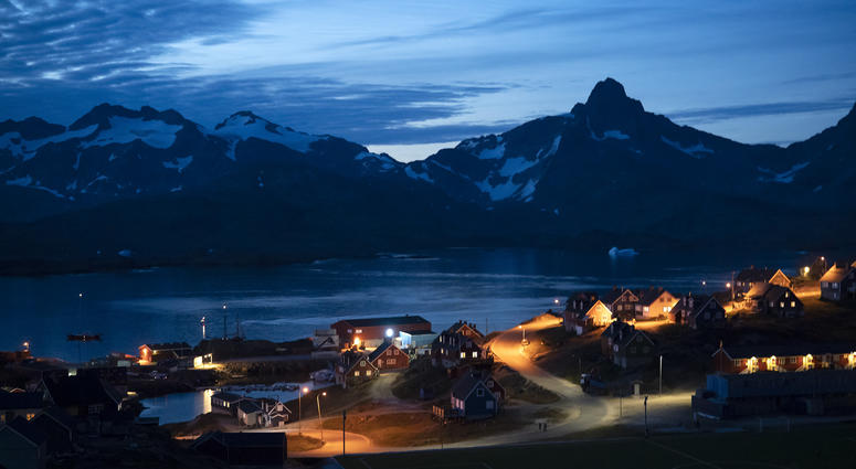 In this photo taken late Friday, Aug. 16, 2019, homes are illuminated after the sunset in Tasiilaq, Greenland. Greenland