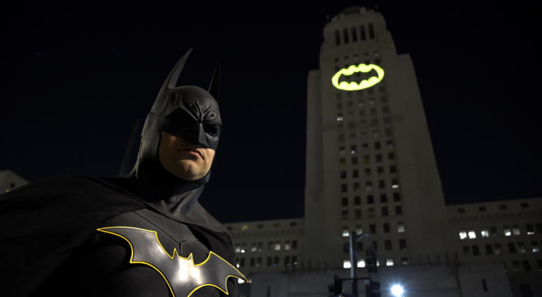 Tony Bradshaw, of Los Angeles, dressed as Batman, poses in front of a Bat-Signal projected onto City Hall during a tribute to "Batman" star Adam West in Los Angeles on June 15, 2017.