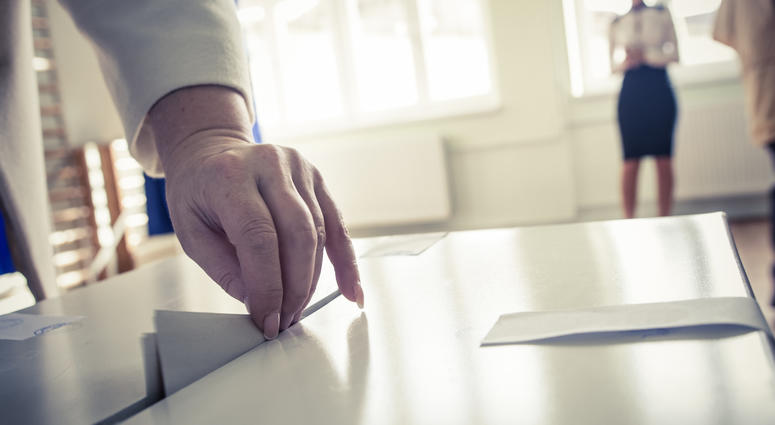 Hand of a person casting a ballot at a polling station during voting. Paper Ballot