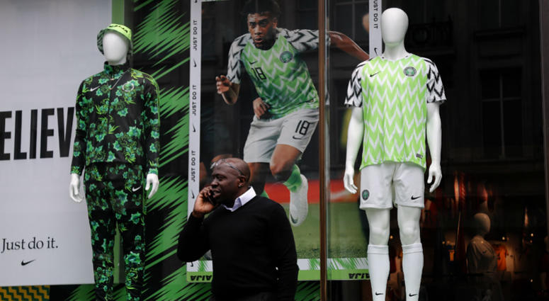 In this June 5, 2018 photo a man stands in front of a Nigerian national soccer team jersey is on display at a shop in London. With just days to go before the FIFA World Cup, some winners and losers have emerged among the often wild and wacky team jerseys. a man stands in front of a Nigerian national soccer team jersey is on display at a shop in London