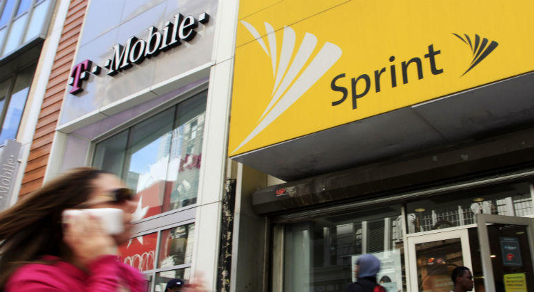 April 27, 2010 file photo, a woman using a cell phone walks past T-Mobile and Sprint stores in New York. Woman walks past T-Mobile and Sprint stores in New York