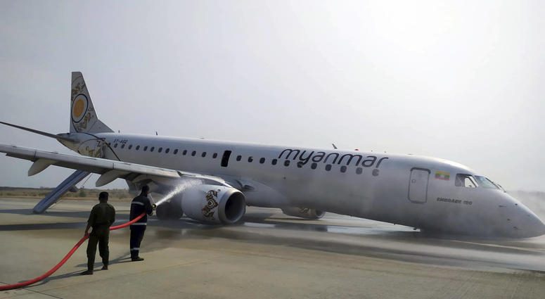 Firefighters work with hose on a plane of Myanmar National Airline (MNA) after an accident at Mandalay International airport Sunday, May 12, 2019, in Mandalay, Myanmar. All passengers and crew are reported safe and uninjured after a Myanmar National Airlines plane made a scheduled but emergency landing at Mandalay International Airport on only its rear landing wheels.