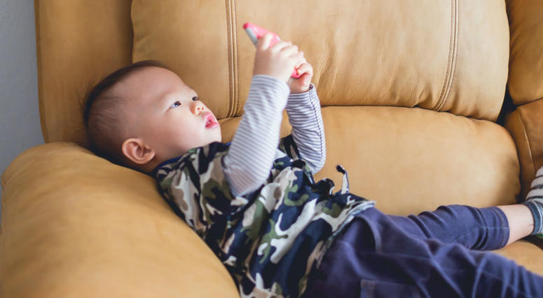 1 year old baby boy child sitting on sofa watching a video from smart phone. 1 year old baby boy child sitting on sofa watching a video from smart phone.