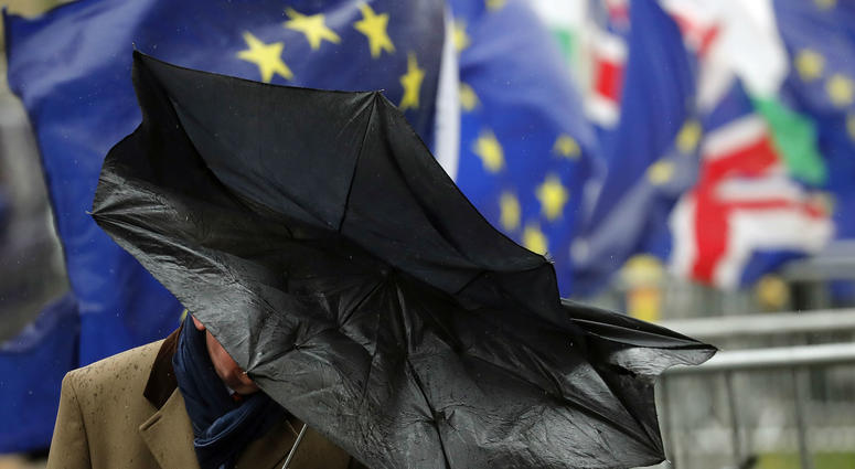 A man shelters with an umbrella as he walks by Pro EU protestors holding flags opposite the Houses of Parliament in London, Thursday, April 4, 2019. A man shelters with an umbrella as he walks by Pro EU protestors holding flags opposite the Houses of Parliament in London, Thursday, April 4, 2019.