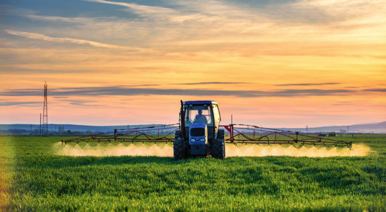 Farming tractor plowing and spraying on field at sunset Farmers