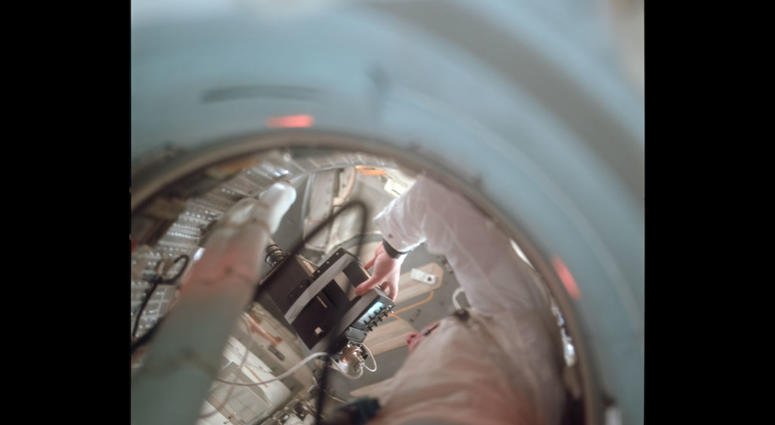 View up the tunnel towards the LM showing Neil holding the TV camera. Note how the small TV monitor has been taped to the camera body. View up the tunnel towards the LM showing Neil holding the TV camera. Note how the small TV monitor has been taped to the camera body.