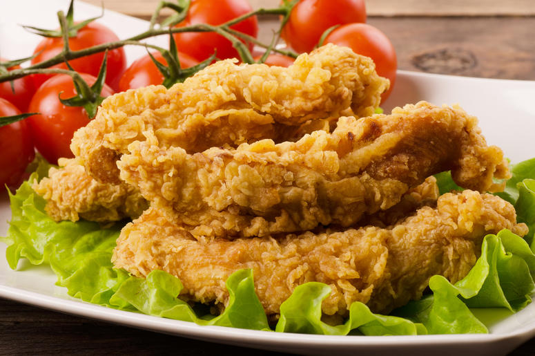 Chicken Strips Golden fried chicken strips in breading with salad and tomatoes on a white plate (Photo credit: Aperturesound/Dreamstime)