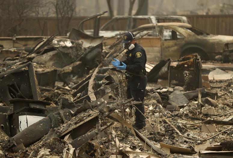 A Sheriff's deputy looks for human remains at a home burned in the Camp fire in Magalia, Calif. California Wildfires