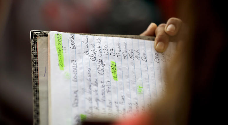 In this Oct. 23, 2018 image, a woman holds the book of numbers and names as she calls those that will be allowed to cross the border and request asylum in the United States, in Tijuana, Mexico. Mexico Border